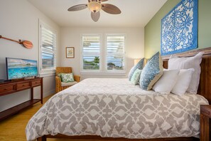 Une chambre à coucher avec un lit, un ventilateur de plafond, une télévision et une fenêtre avec des stores.