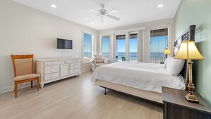 A bedroom with a bed, a chair, a dresser, a television, and a balcony with a view. - Sea Monster, East. Pool. Extra fridges. Lots of space. And right on the beach! (Gulf Shores)
