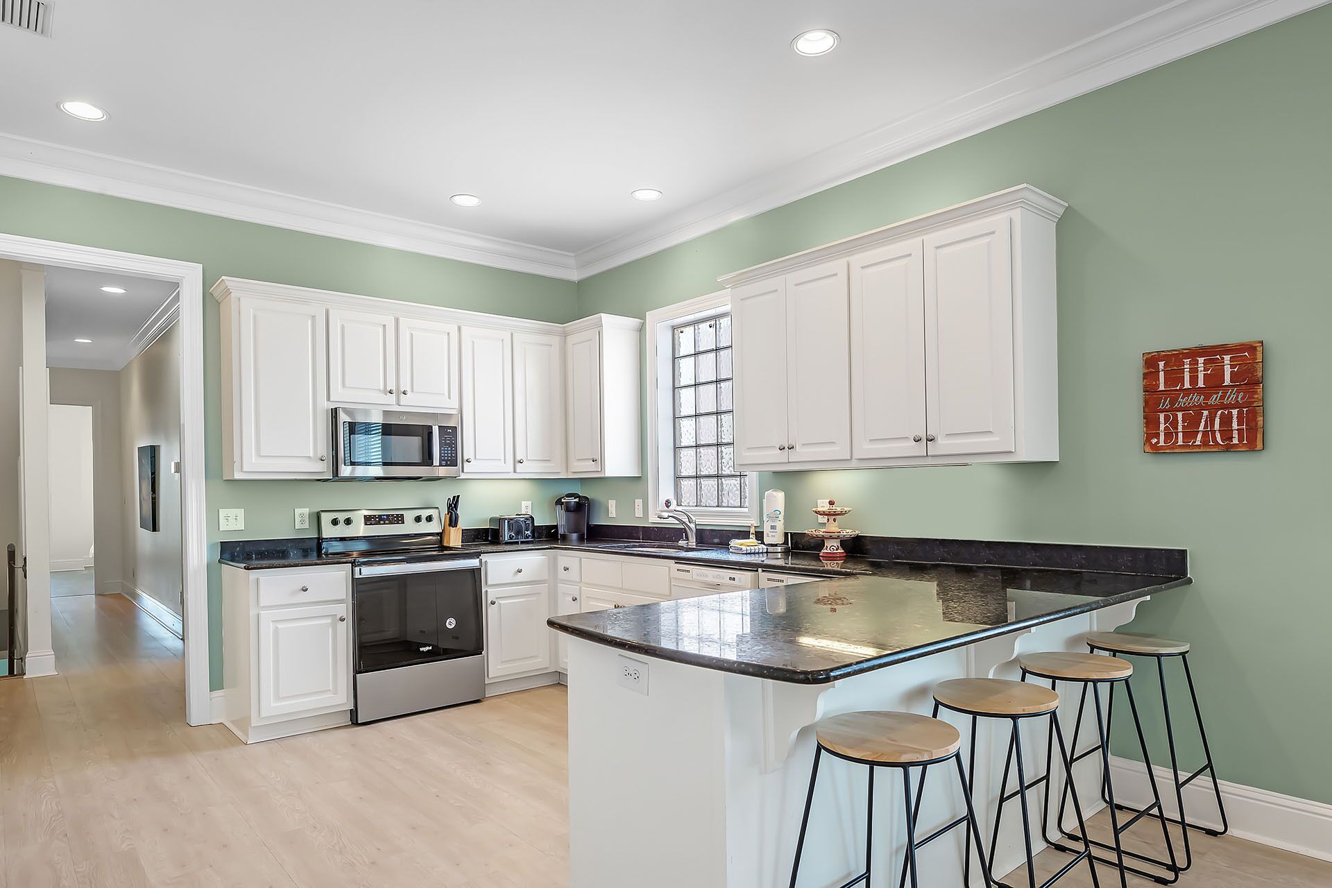 A modern kitchen with white cabinets, a central island with stools, a microwave, and a coffee maker.