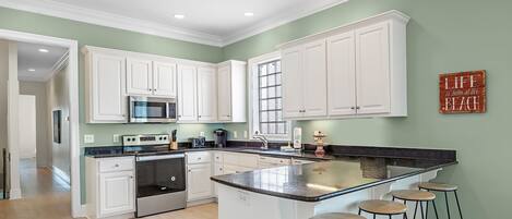 A modern kitchen with white cabinets, a central island with stools, a microwave, and a coffee maker.