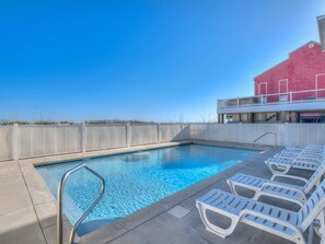 A swimming pool with a clear blue sky, a white fence, and lounge chairs. - Sea Monster, East. Pool. Extra fridges. Lots of space. And right on the beach! (Gulf Shores)