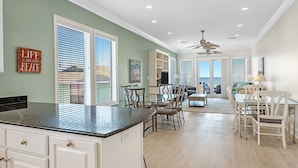 A spacious kitchen with a large island, dining area with white chairs, and a view of the ocean through the sliding glass doors. - Sea Monster, East. Pool. Extra fridges. Lots of space. And right on the beach! (Gulf Shores)