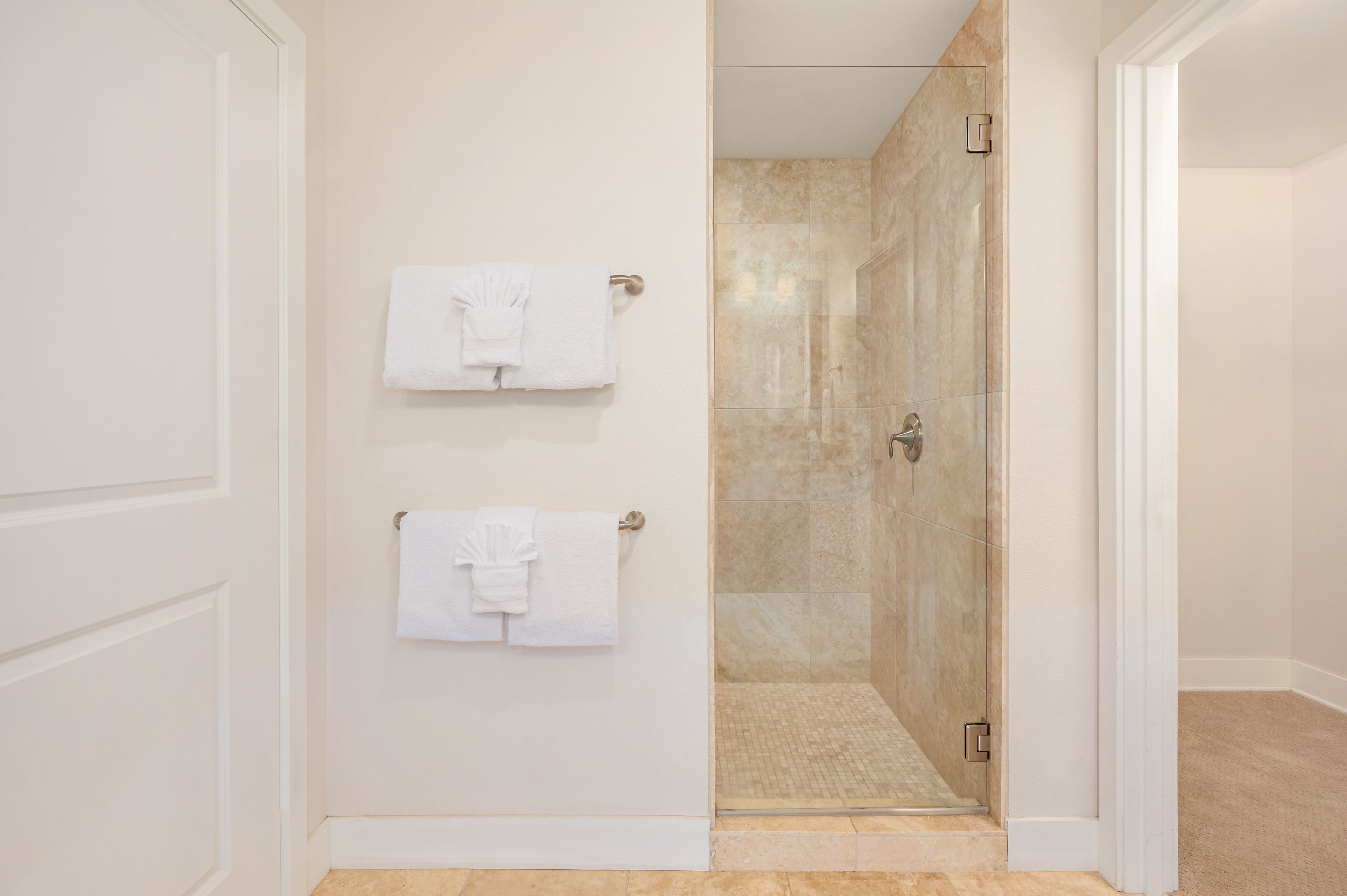 Un baño con dos toallas blancas colgadas en una pared, una cabina de ducha de vidrio y un suelo de baldosas beige.