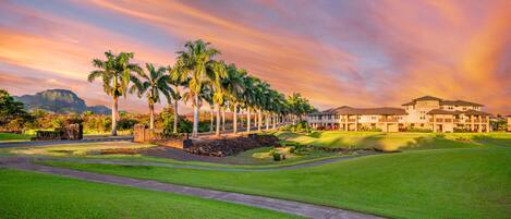 A golf course with a clubhouse, palm trees, and a mountainous backdrop.