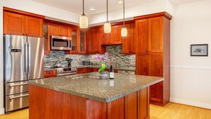 A modern kitchen with wooden cabinets, stainless steel appliances, a granite countertop, and pendant lighting.