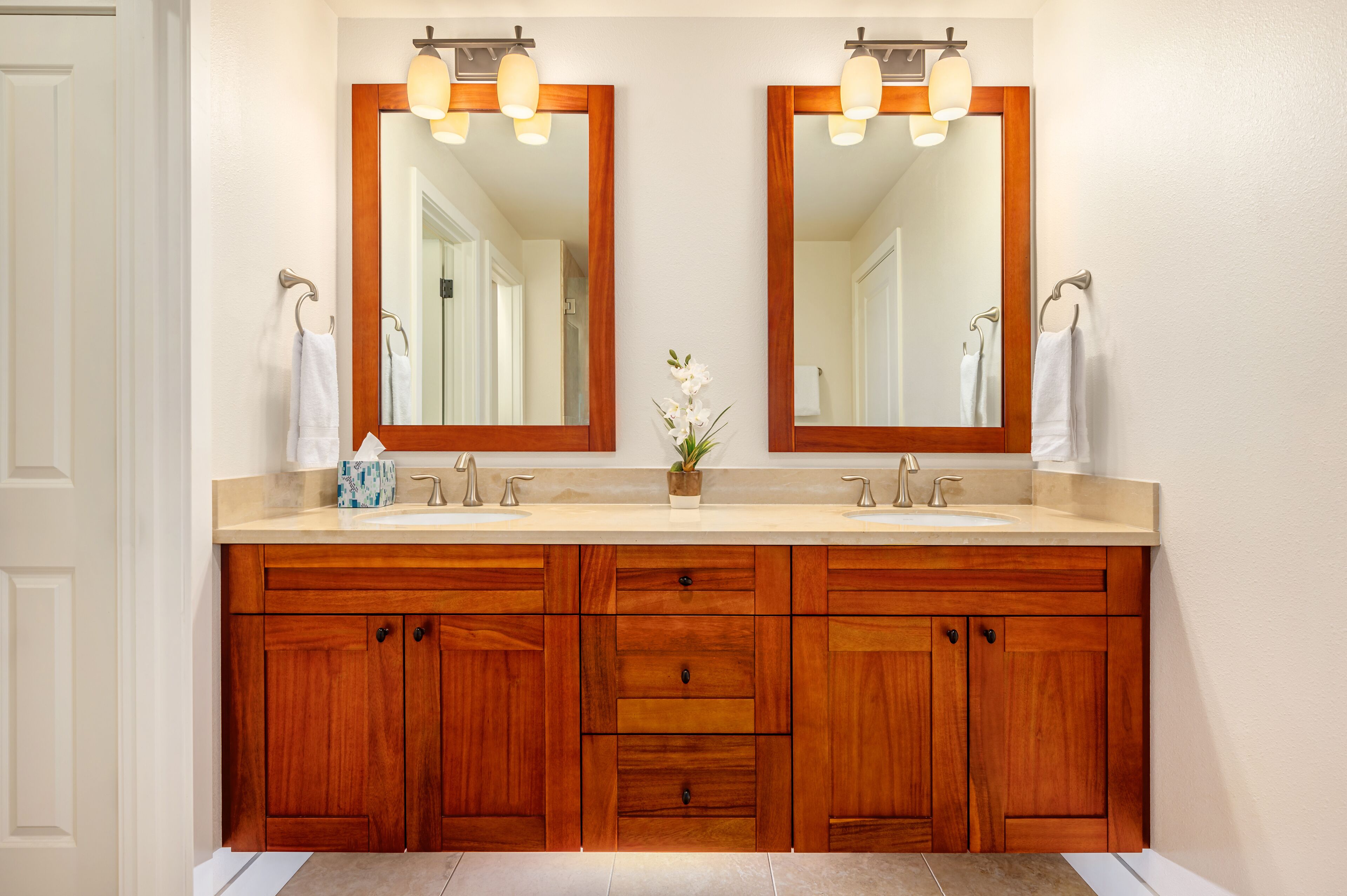 A bathroom with a double vanity, wooden cabinets, a mirror, and a small potted plant.