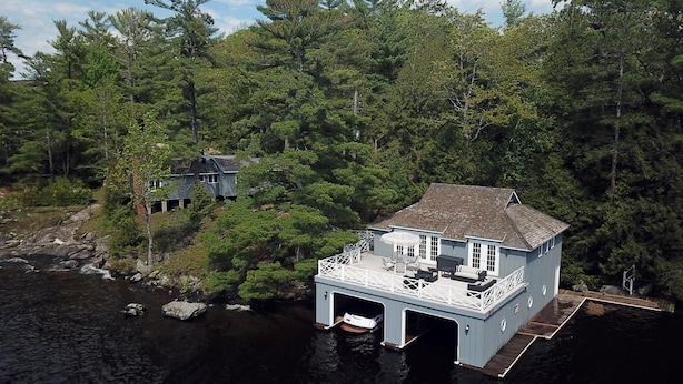 A house with a dock extending into a lake, surrounded by dense forest.