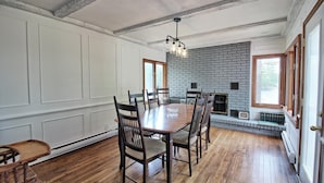 A dining room with a wooden table and chairs, a brick fireplace, and a window with a view.