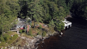 An aerial view of a house with a dock extending into a river, surrounded by dense forest.