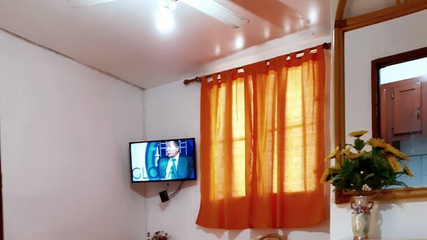Een hotelkamer met een bed, een bureau, een stoel, een aan de muur bevestigde televisie en een raam met oranje gordijnen.