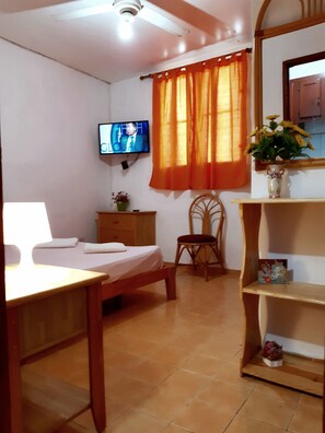 Habitación de hotel con cama, escritorio, silla, televisor montado en la pared y ventana con cortinas naranjas.