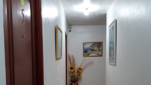 Een gang met een houten deur, een vaas met zonnebloemen en een schilderij aan de muur.
