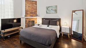 Een moderne slaapkamer met een bakstenen open haard, een flatscreen televisie, een groot bed, bedlampjes en een spiegel.