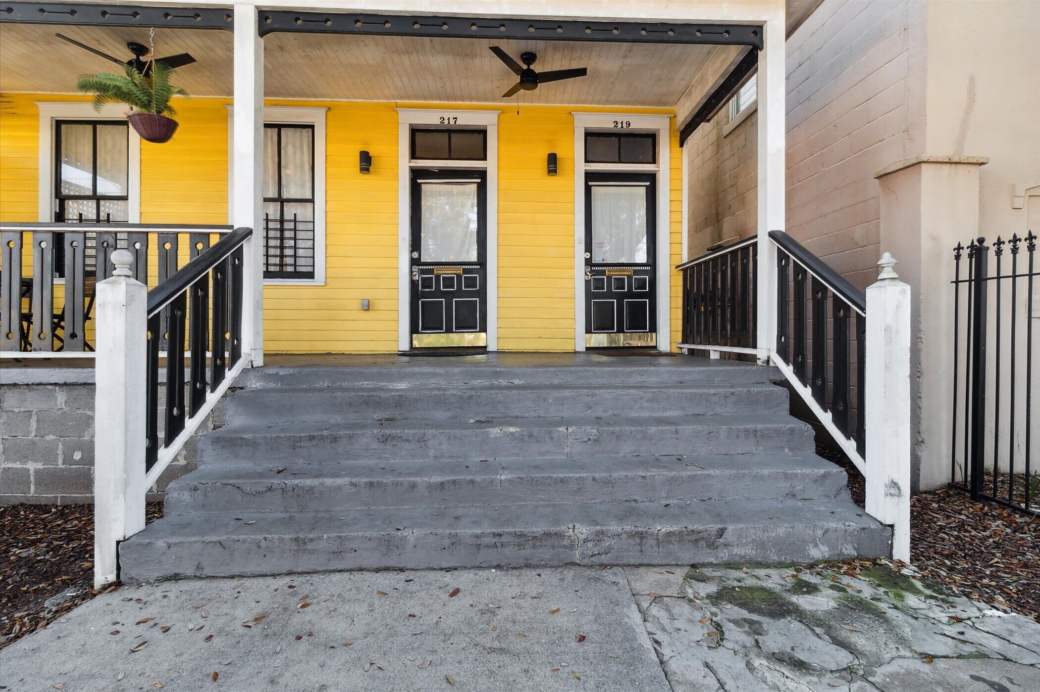 Un bâtiment jaune avec deux portes noires, numérotées 217 et 219, et un escalier en béton menant à l’entrée.