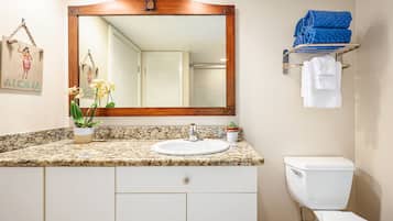 Un baño con encimera de granito, un lavabo blanco, un espejo, inodoro y un perchero con toallas dobladas.
