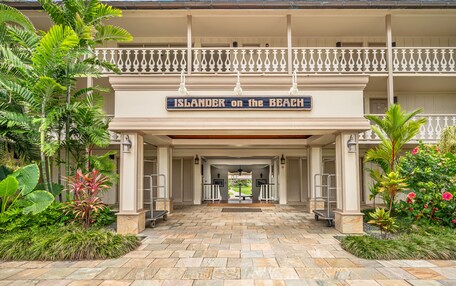 Entrada de hotel con un letrero que dice "Islander on the Beach", que presenta un corredor cubierto, piso de piedra y jardines tropicales.