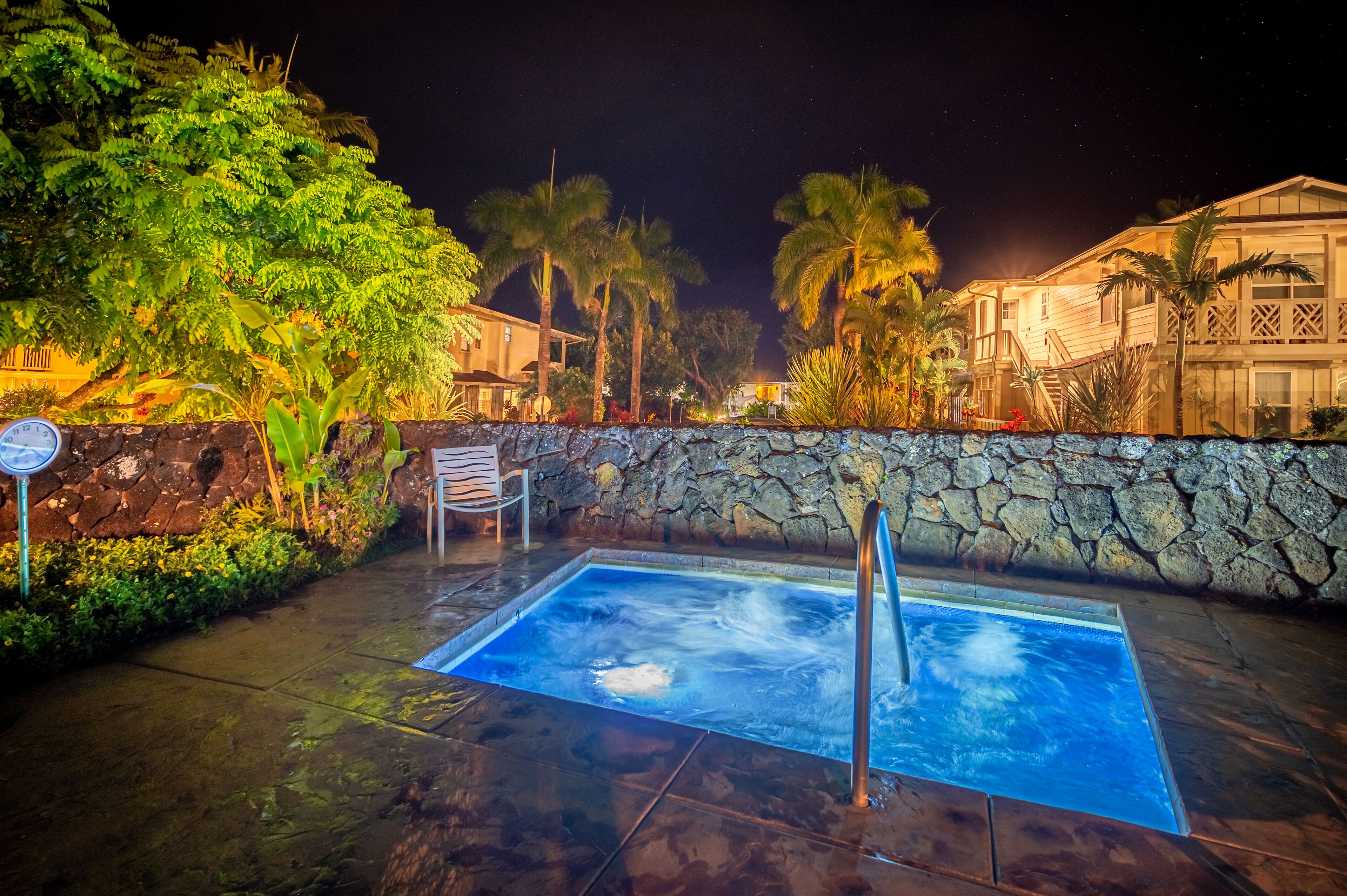 A heated outdoor pool with a stone wall and palm trees in the background.