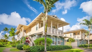 Une maison à deux étages dotée d’un balcon, entourée d’une végétation luxuriante et de palmiers.