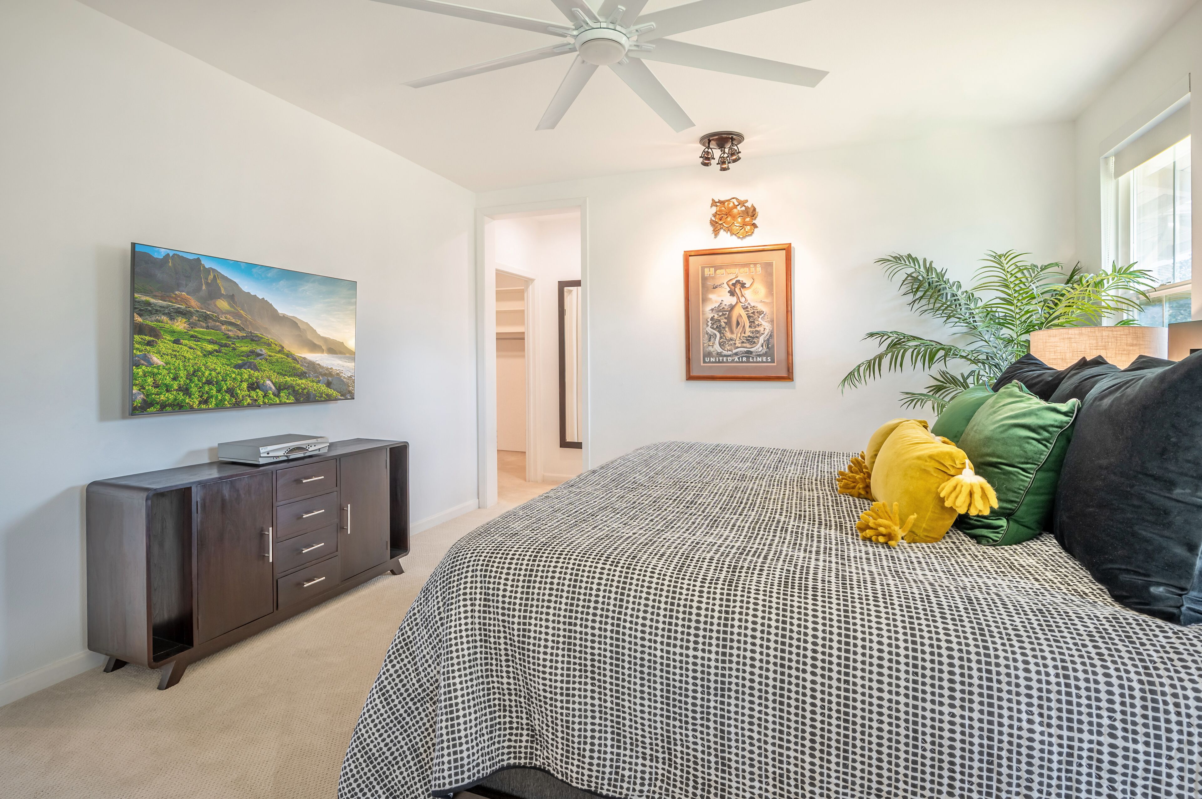 Une chambre à coucher avec un lit, une commode, un tableau, une photographie encadrée et une plante.