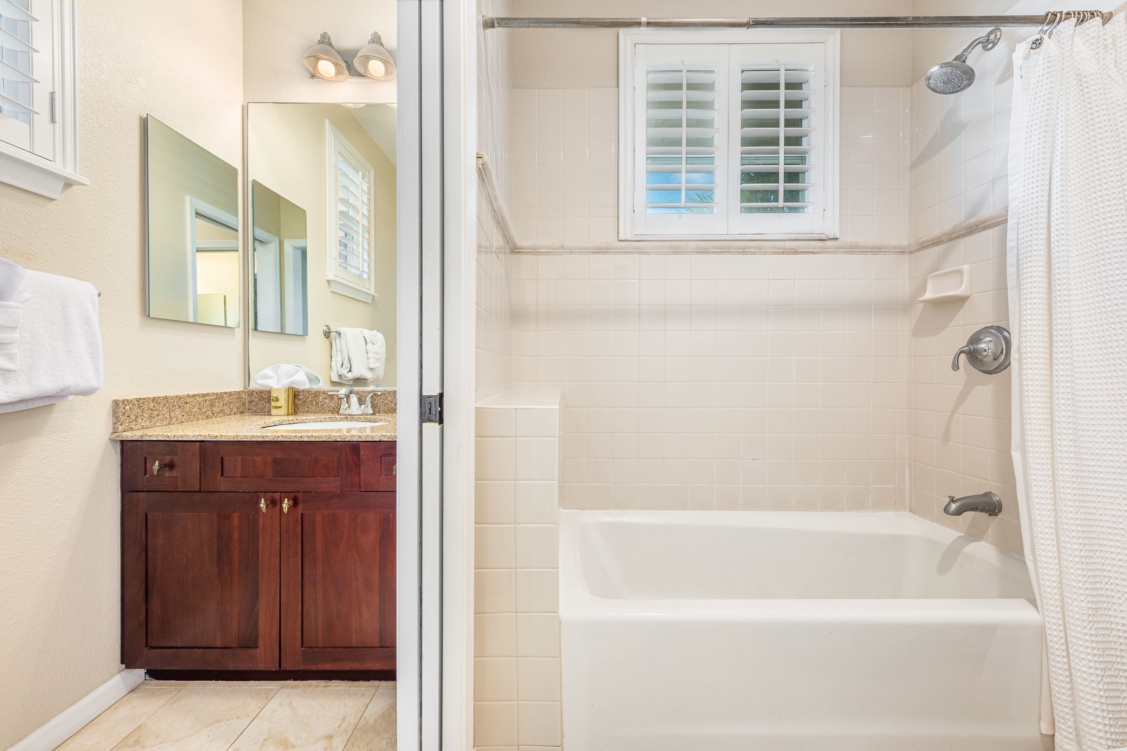 A bathroom with a bathtub, a shower, a vanity with a mirror, and a window with blinds.