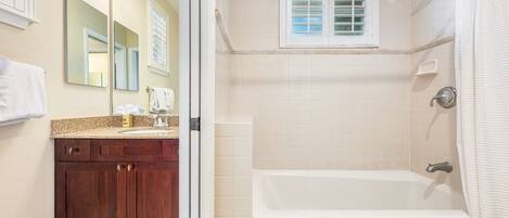 A bathroom with a bathtub, a shower, a vanity with a mirror, and a window with blinds.