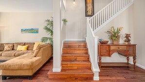 Una escalera con escalones de madera y barandillas blancas que conduce a una zona de descanso con una mesa consola de madera y una planta en maceta.