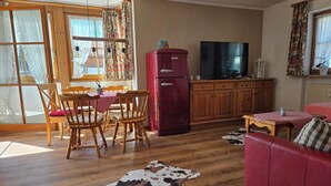 Una sala de estar acogedora con un sofá rojo, una mesa de comedor de madera con sillas, un refrigerador rojo, un televisor y un tapete de cuero de vaca.