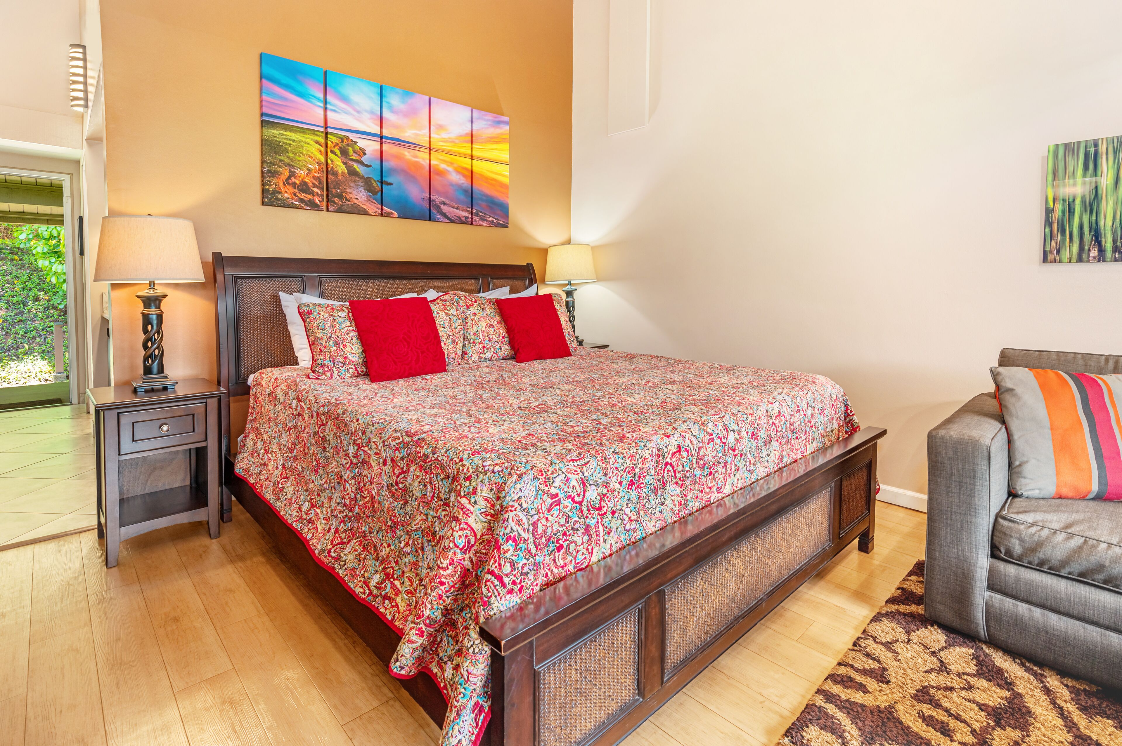 Une chambre avec un grand lit, deux tables de chevet, un canapé gris et un tapis à motifs.