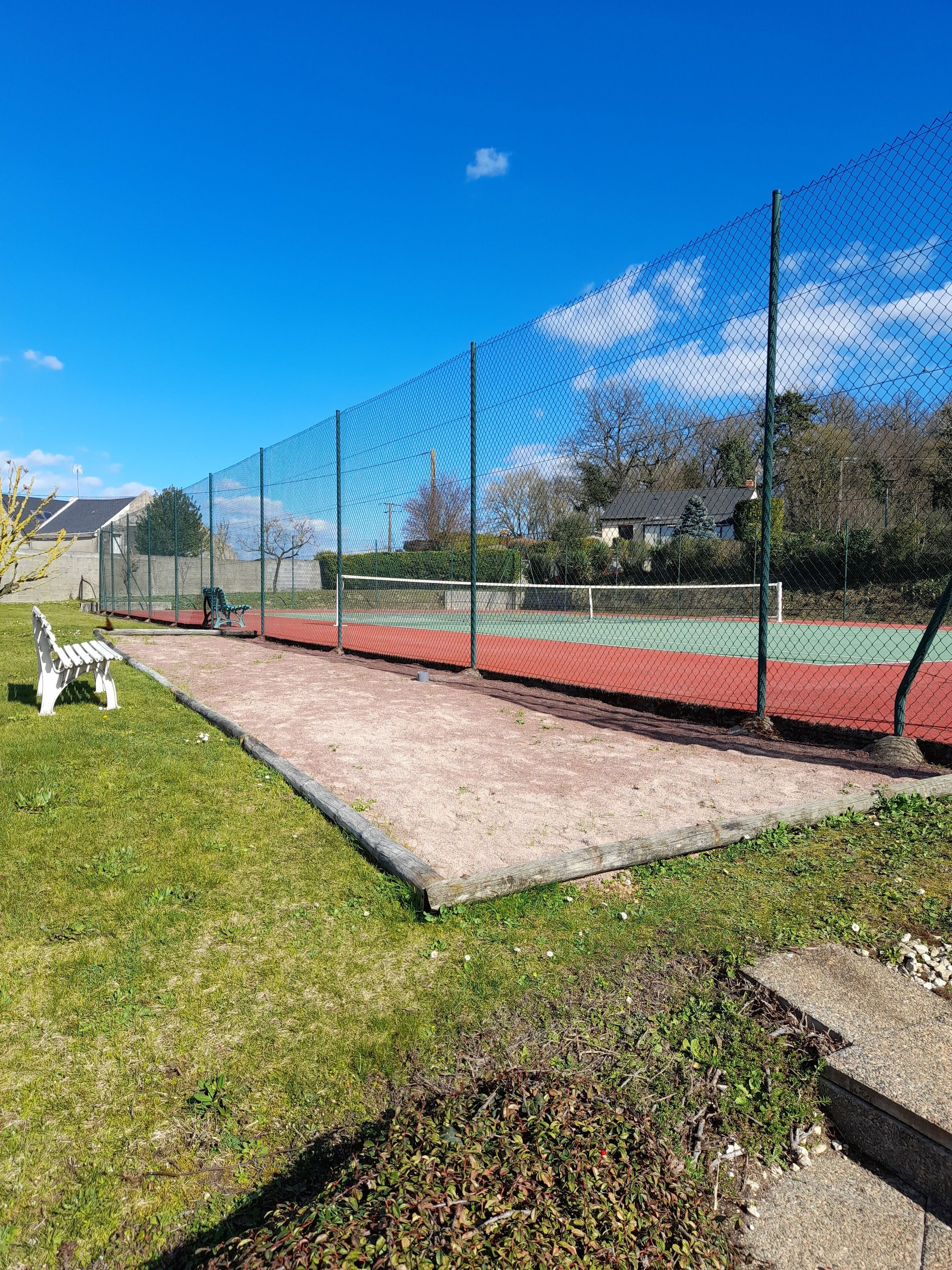 En tennisbane med hegn, bænk og græsplæne.