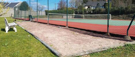 En tennisbane med hegn, bænk og græsplæne.
