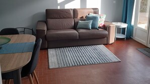 A modern living room with a brown leather sofa, a small round table, and a patterned rug. - Gite le Clos Ferré SWIMMING POOL TENNIS (Brézé)