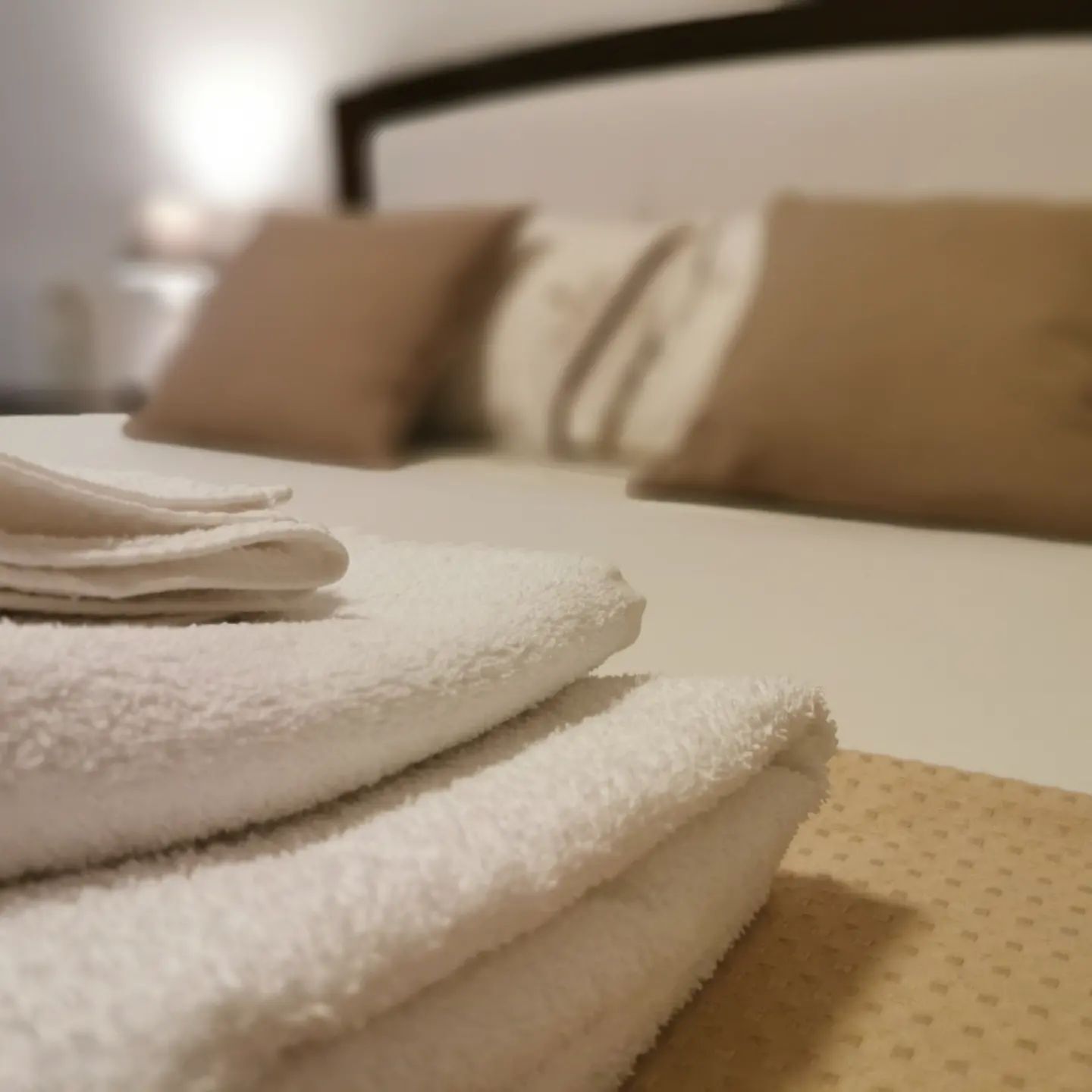 A neatly folded stack of white towels on a bed with a headboard.