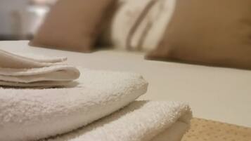A neatly folded stack of white towels on a bed with a headboard.
