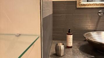 A bathroom with a glass shower enclosure, a sink with a round basin, and a mirror with an ornate frame.