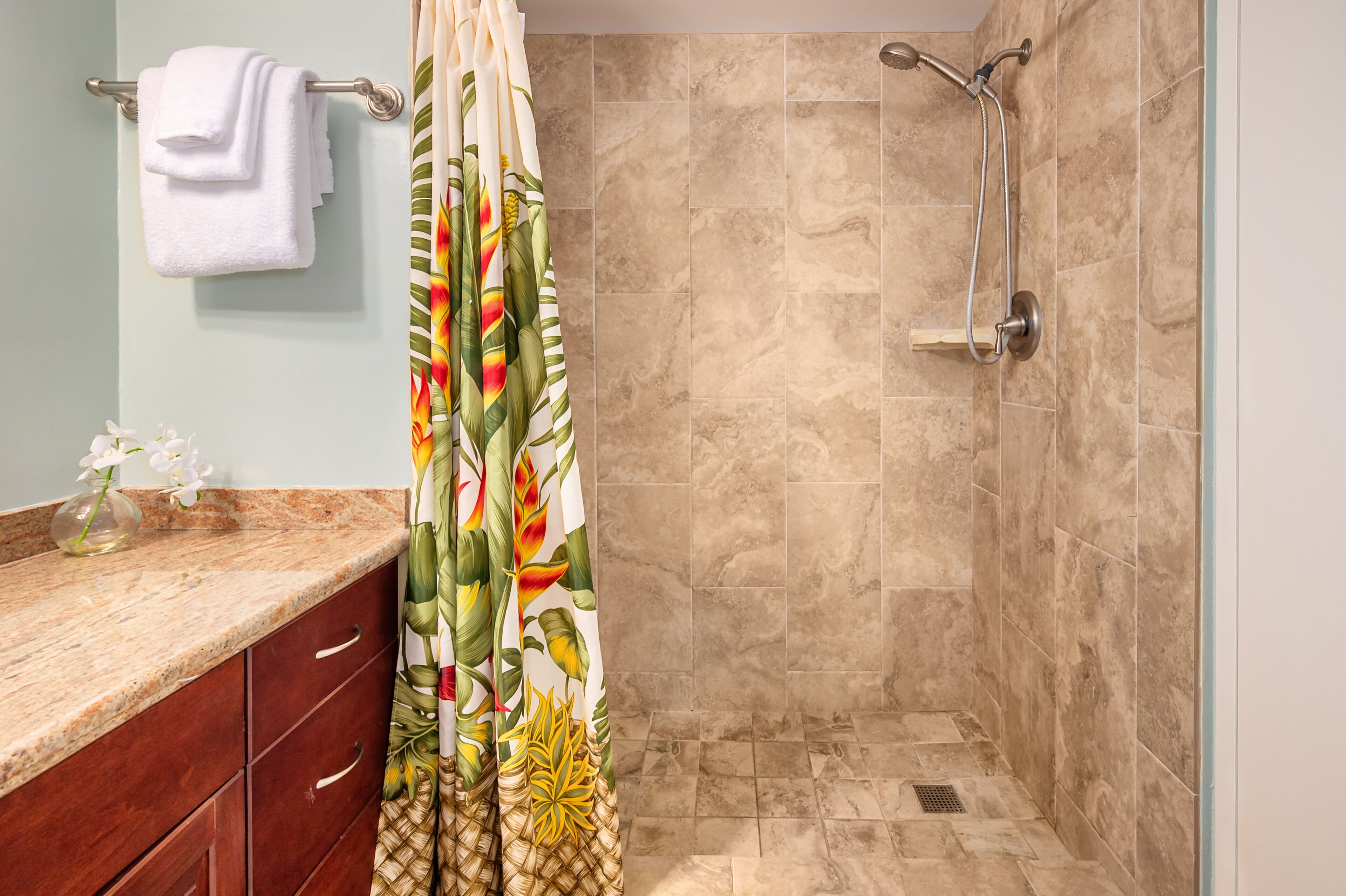 A bathroom with a shower, a towel rack, a sink with a vase of flowers, and a decorative shower curtain.