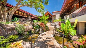 Un jardin tropical avec un sentier en pierre, de gros rochers et diverses plantes tropicales.