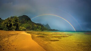 Une plage avec un arc-en-ciel, une eau cristalline et une montagne en arrière-plan.