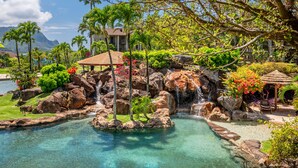 Un complexe hôtelier tropical doté d’une piscine à eau cristalline, de palmiers, d’une cascade et offrant une vue sur la plage.