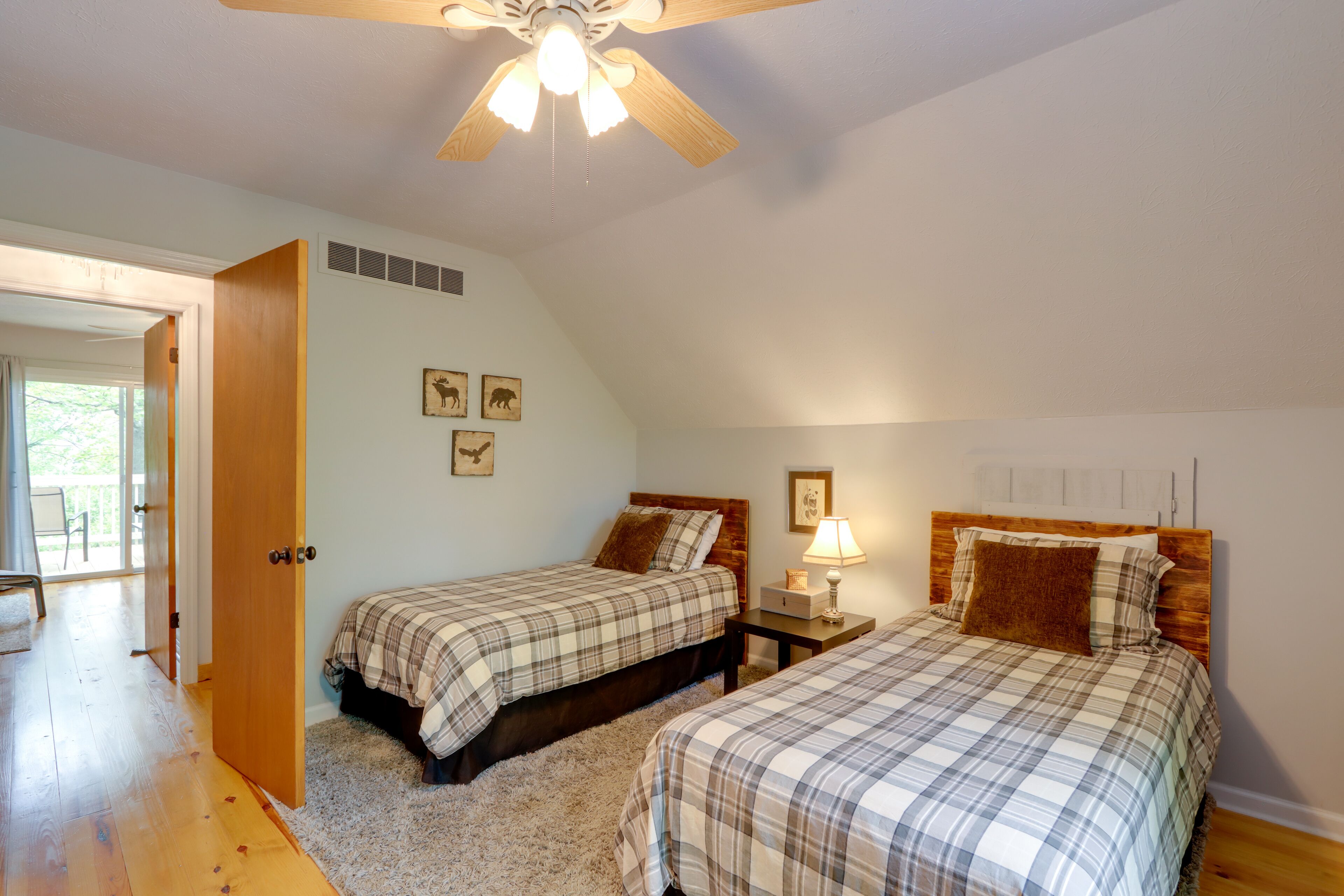 A bedroom with two beds, a ceiling fan, a nightstand with a lamp, and a door leading to a balcony.