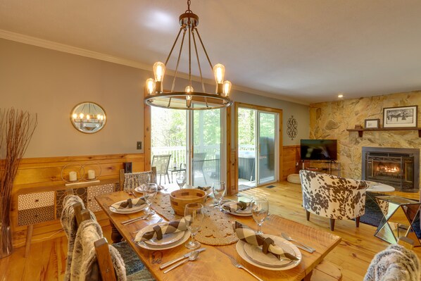 A dining area with a wooden table set for four, a chandelier, and a fireplace in the background. - Blue Ridge Getaway w/ Hot Tub & Seasonal View! (Blue Ridge)
