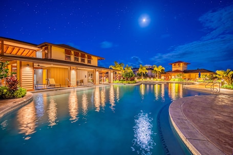 A nighttime view of a resort with a swimming pool, multiple buildings, and palm trees.