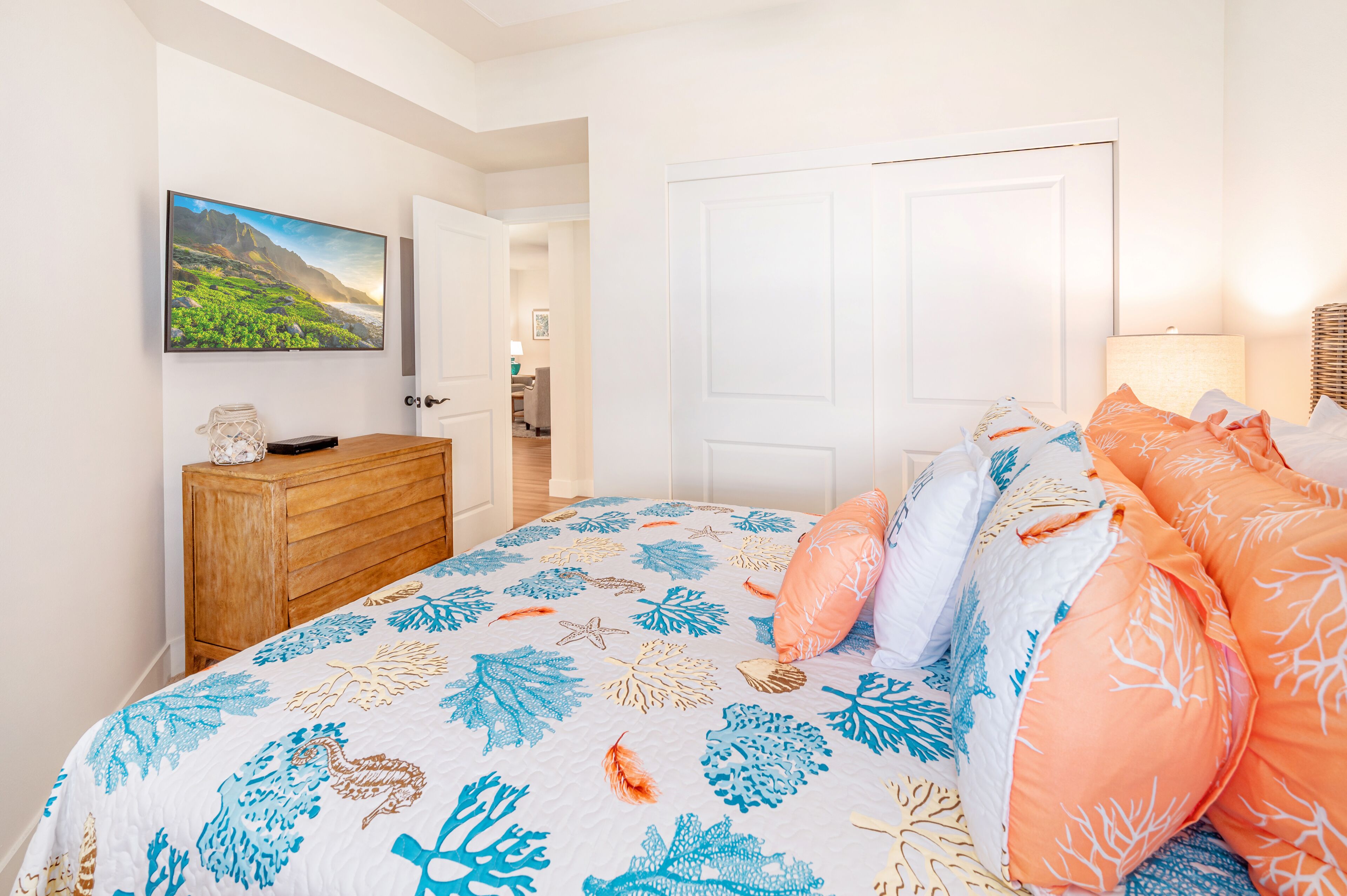 A bedroom with a bed, a dresser, a door, and a wall-mounted TV.