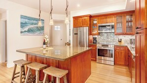 A modern kitchen with wooden cabinets, stainless steel appliances, and a large island with stools. - Pili Mai Family Condo 5C, 3 Bedroom 3 Bath, Mountain View, Cool Lanai, (Koloa)