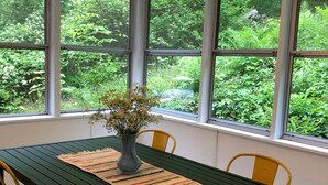En matplats med ett bord, stolar och utsikt över grönskan genom stora fönster.