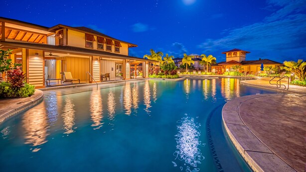 Vue nocturne d’un complexe hôtelier avec une piscine, plusieurs bâtiments et des palmiers.
