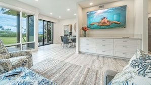 A spacious living area with a large flat-screen TV, a dining table, and a view of the outdoors.