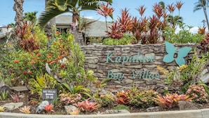 A sign for Kapalua Bay Villas with a stone wall and tropical plants.
