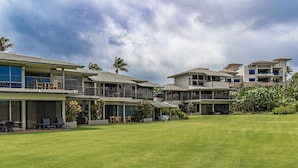 A modern multi-story residential building with balconies, a covered patio, and a well-maintained lawn.