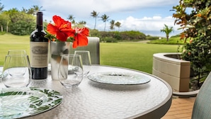 A table set outdoors with a bottle of wine, glasses, and a vase with a red flower.