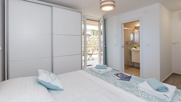 Un dormitorio con cama, mesita de noche, armario y baño visible a través de una puerta abierta.